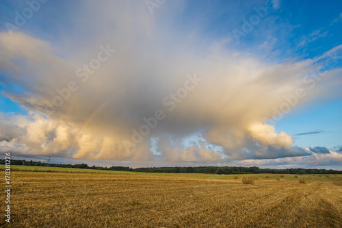 Finite field after harvest, rainbow over a field of straw bales