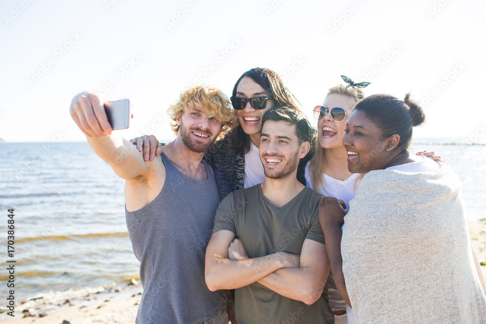 Friendly girls and guys making selfie on seashore during travel