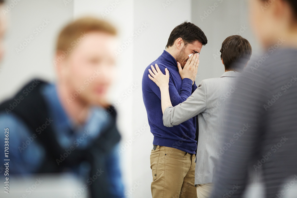 Young man crying while groupmate touching his shoulder and sharing his pain Young man crying while groupmate touching his shoulder and sharing his pain