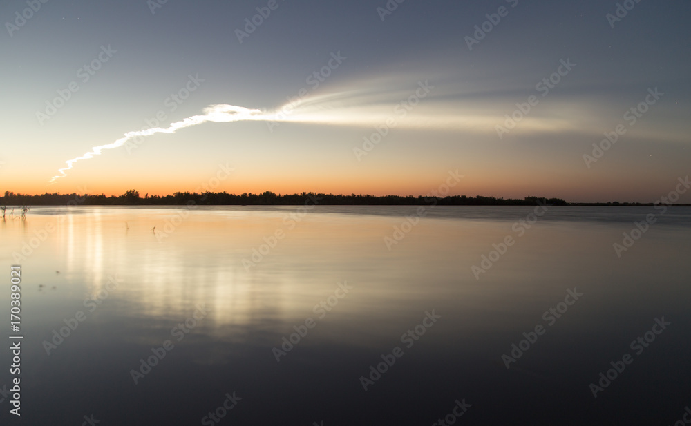 Smoke trail from a rocket at sunset with reflection in water