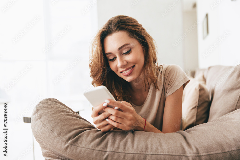 Happy emotional pretty lady lies on sofa chatting by phone.