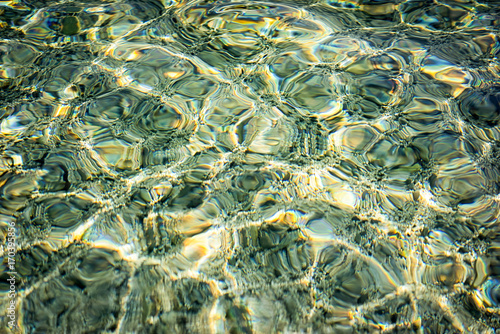 texture of sunlight at the water surface at the sea pebble shore.