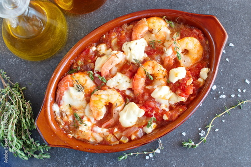 Oven backed prawns with feta, tomato, paprika, thyme in a traditional ceramic form on a abstract background. Healthy eating concept. Mediterranian lifestyle.