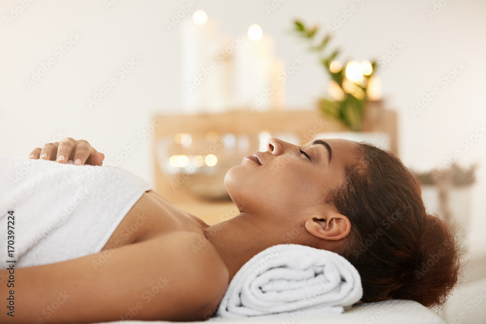Beautiful african girl lying in spa salon with closed eyes.