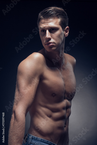 one young adult man, Caucasian, fitness model, muscular body, shirtless, jeans, black background, studio, posing, looking sideways
