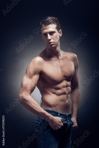 one young adult man, Caucasian, fitness model, muscular body, shirtless, jeans, black background, studio, posing, looking sideways