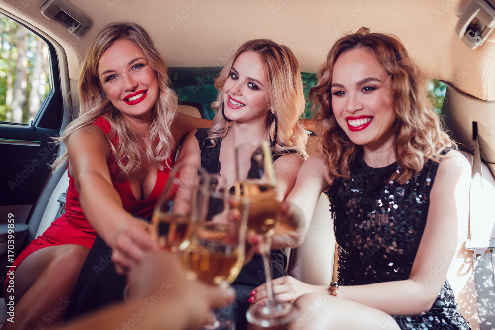 Pretty women having party in a limousine car and drinking champagne.