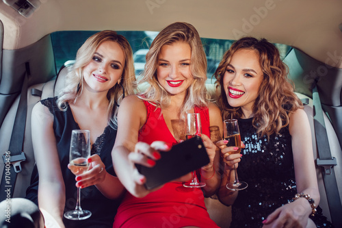 Women drinking champagne and make selfie in a limousine car.
