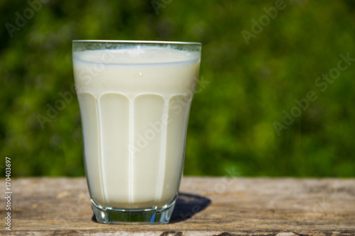 Glass of milk on wooden table with nature background