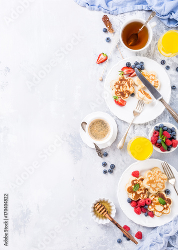 Flat lay with breakfast with scotch pancakes in flower form, berries and honey on light wooden table. Healthy food concept with copy space.