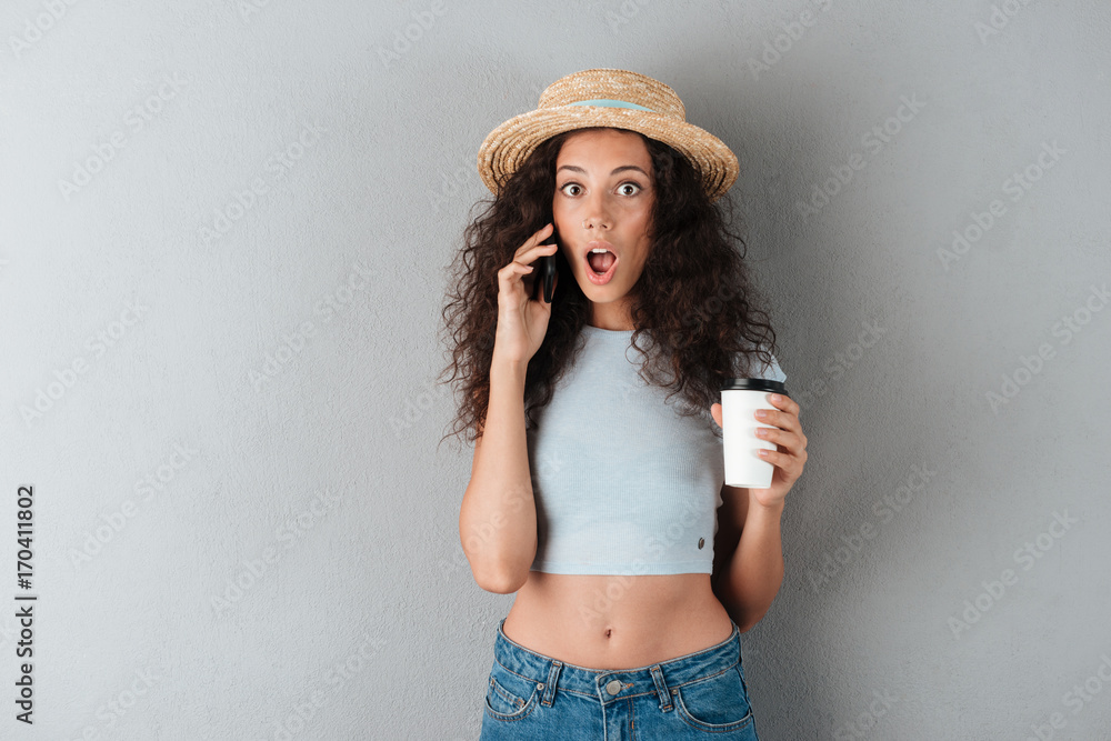 Shocked curly woman in hat talking by the smartphone Shocked curly woman in hat talking by the smartphone
