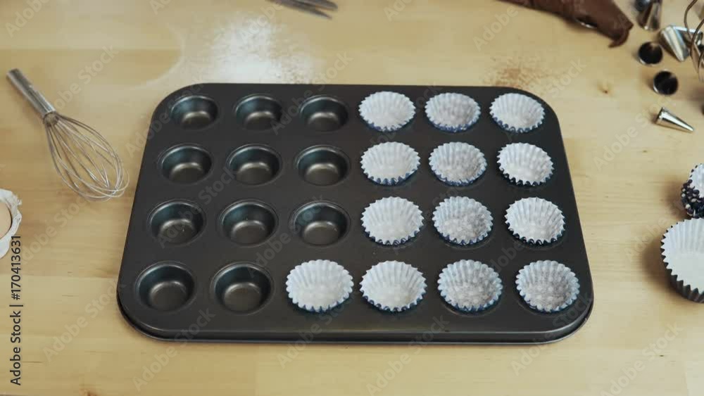 Close-up view of female hand putting the wrappers paper cups into the baking dish. Woman cooking cupcakes. Time lapse. Close-up view of female hand putting the wrappers paper cups into the baking dish. Woman cooking cupcakes. Time lapse.