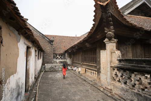 Yard of ancient village communial house with little girl wearing traditional dress Ao Dai running on ground