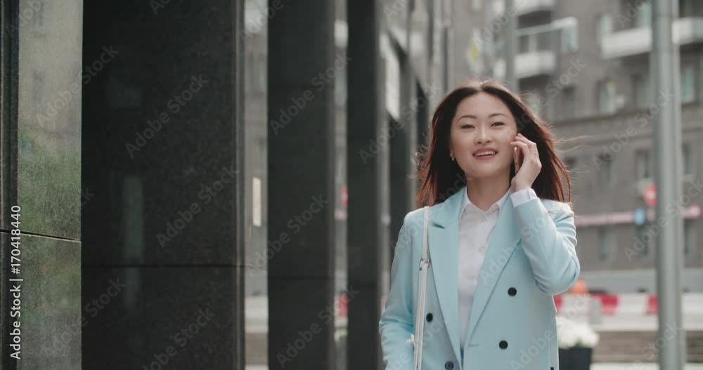 Steadicam shot of a young beautiful Asian girl in a great mood, emotionally speaks on the phone on the way to work Steadicam shot of a young beautiful Asian girl in a great mood, emotionally speaks on the phone on the way to work