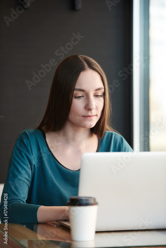 Young woman working on laptop while sitting at cafe