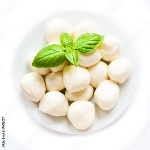 Bowl of small mozzarella balls isolated on white background with basil leaves,  close up, top view.