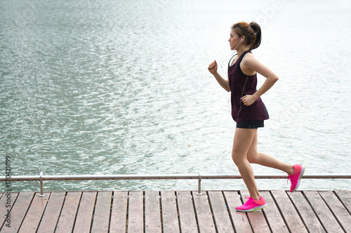 Asian sport woman jogging on lake rim in park for health