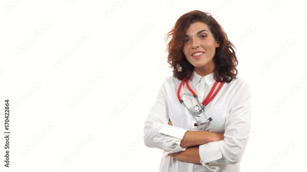 Young female doctor walking in, smiling friendly, crossing arms and looking at camera. Portrait of young medical professional with stethoscope and lab coat isolated on white background Young female doctor walking in, smiling friendly, crossing arms and looking at camera. Portrait of young medical professional with stethoscope and lab coat isolated on white background