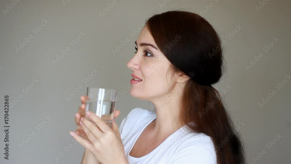 Happy young woman drinks a glass of water to stay healthy. Girl drinking and smiling. Close-up Happy young woman drinks a glass of water to stay healthy. Girl drinking and smiling. Close-up