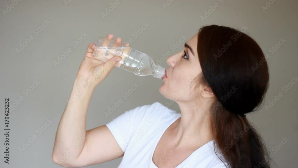 Happy young woman drinks a glass bottle of water to stay healthy. Girl drinking and smiling. Happy young woman drinks a glass bottle of water to stay healthy. Girl drinking and smiling.