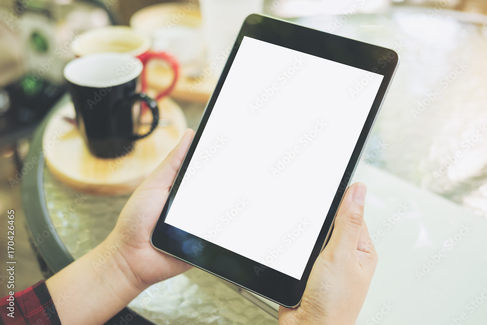 Mockup image of hands holding black tablet pc with blank white screen with coffee cups on glass table in modern cafe Mockup image of hands holding black tablet pc with blank white screen with coffee cups on glass table in modern cafe