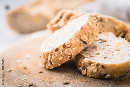 Fresh, healthy whole grain rye baguette and slices on cloth and rustic wooden board, close up. Bakery and grocery concept