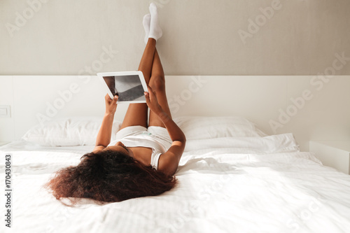 Back view of woman lying in bed with raised legs