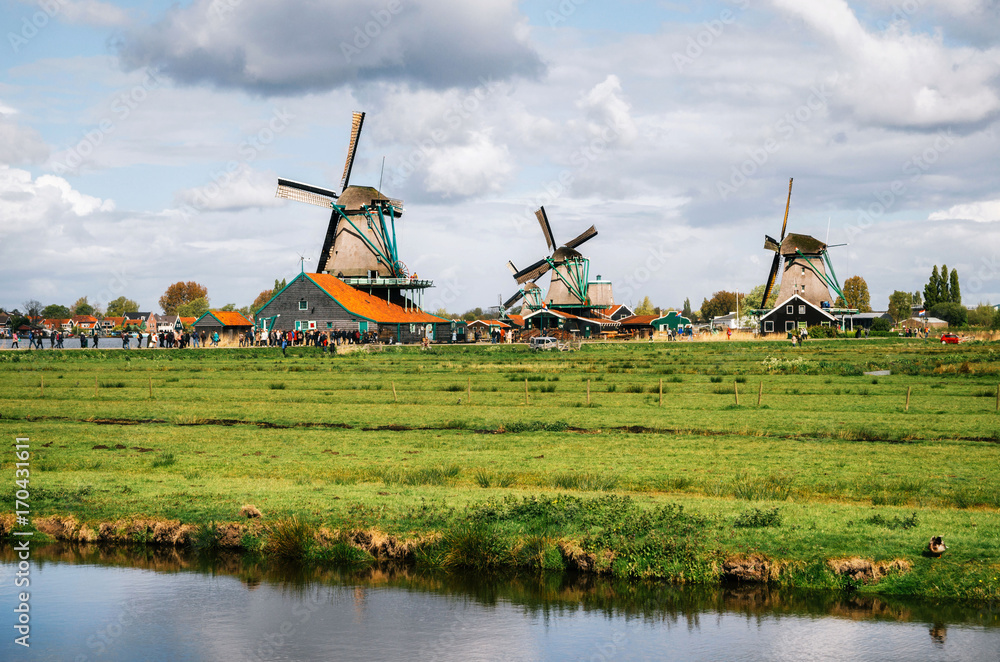 Fototapeta premium Panoramic view of Authentic Zaandam mills in Zaanstad village on the river Zaan against the sky with clouds. Landmark of Netherlands.