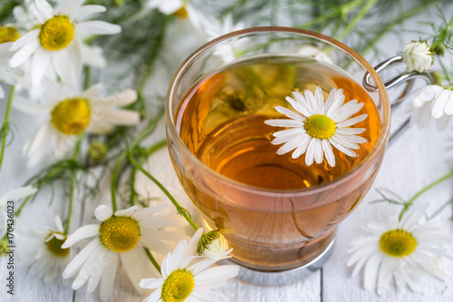 Glass cup of tea with chamomile on white wooden background