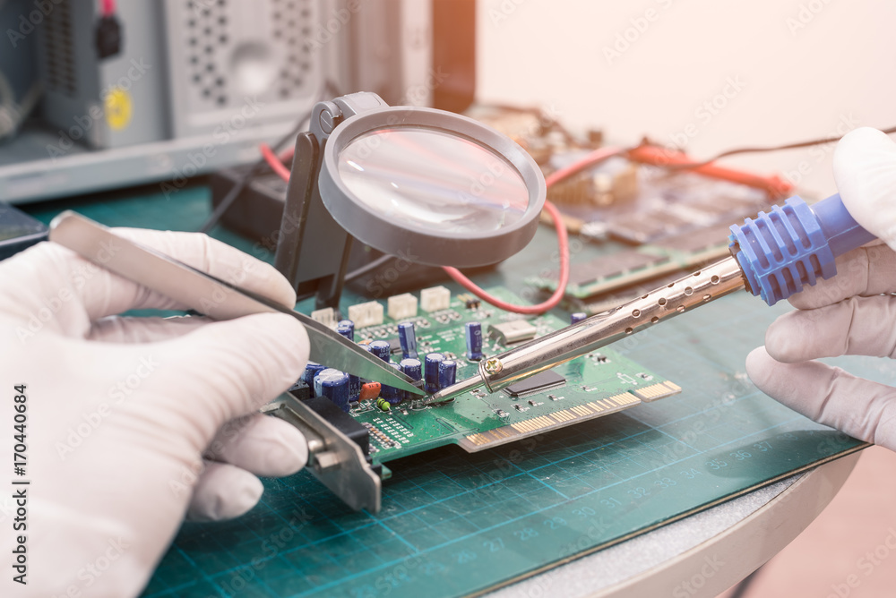 The abstract image of asian technician repairing the computer mainboard by soldering in the lab. The concept of computer hardware, repairing, upgrade and technology. The abstract image of asian technician repairing the computer mainboard by soldering in the lab. The concept of computer hardware, repairing, upgrade and technology.