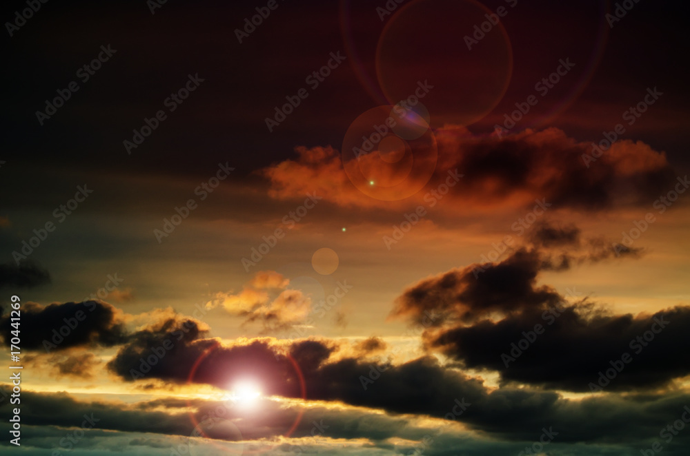 Fototapeta premium Evening sun in the dark sky with cumulus clouds. Bright glare from the sun.