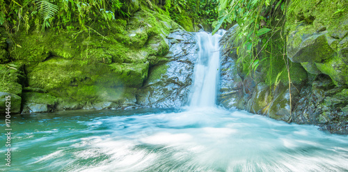 Beautiful small waterfall located inside of a green forest with stones in river at Mindo
