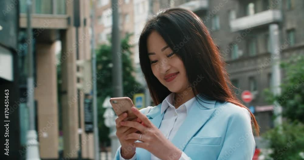 closeup of beautiful young business Asian woman with smartphone smiles and writes messages closeup of beautiful young business Asian woman with smartphone smiles and writes messages