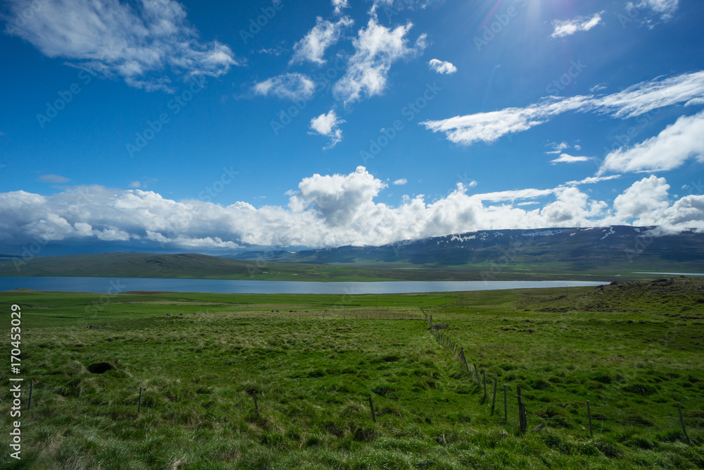 Iceland - Fjord and mountains with snow behind wide green fields