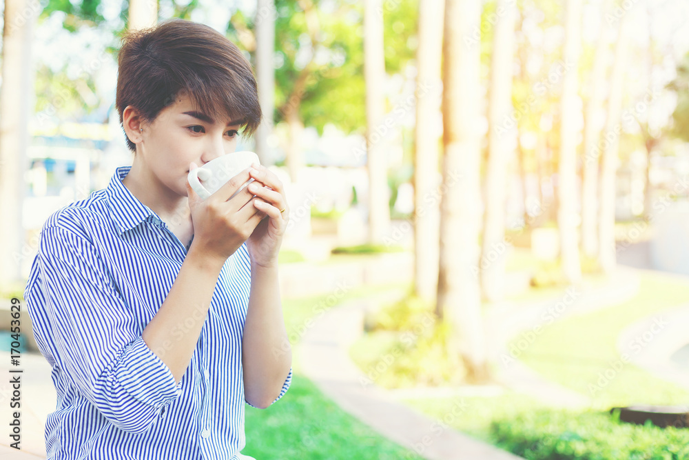 Beautiful short hair woman sitting on the floor and drinking a favorite beverage in white cup between her outdoor working business in the park. Beautiful short hair woman sitting on the floor and drinking a favorite beverage in white cup between her outdoor working business in the park.