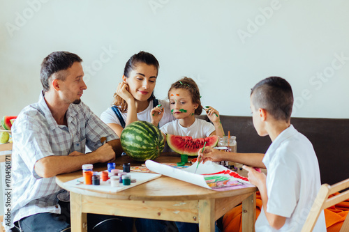 Family with two kids painting together at home, happy mother, father and children. Smiling family drawing together in kitchen at home. New housing, art and family leisure concept. photo
