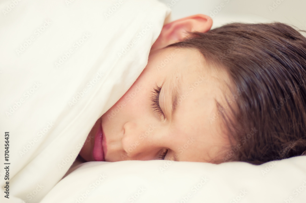 Cute Boy sleeping under a blanket in bed in the bedroom. Lying on bed.  The concept of awakening and the time of sleep. Portrait of a close-up with an instagram filter