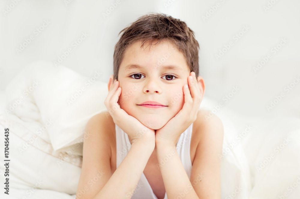 Cute boy under a blanket in bed in the bedroom. Lying on bed. The concept of awakening and the time of sleep. Portrait of a close-up with an instagram filter Cute boy under a blanket in bed in the bedroom. Lying on bed. The concept of awakening and the time of sleep. Portrait of a close-up with an instagram filter