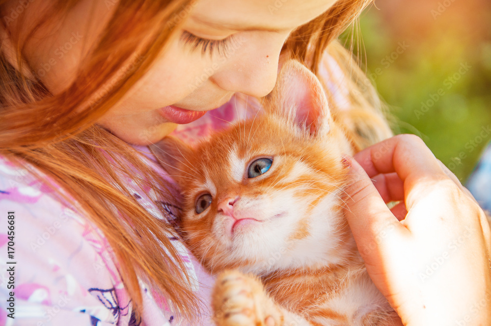 Little girl with a red kitten in hands close up. Bestfriends. Interaction of children with pets.