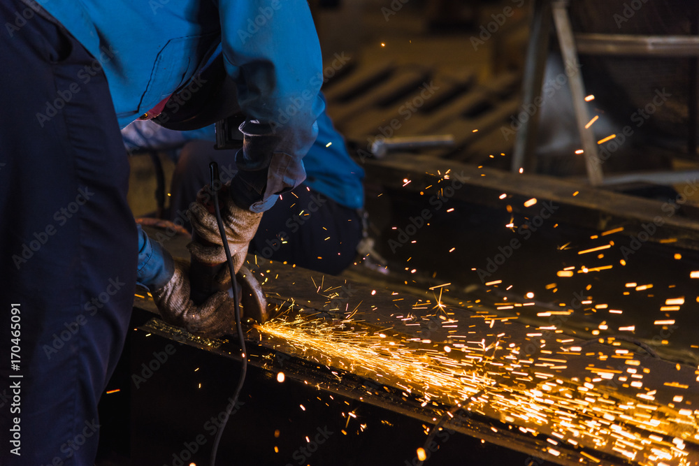 Worker using electric wheel grinding on steel structure in factory. Worker using electric wheel grinding on steel structure in factory.