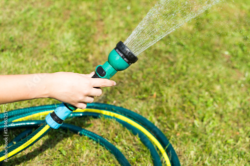 Girl hand spraying water in garden using sprinkler