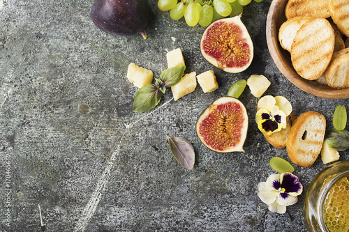Ingredients for appetizing sandwiches for breakfast or snacks from grilled bread, figs, cheese, grapes, honey and nuts on a gray stone background with edible flowers. Top view. © annaileish