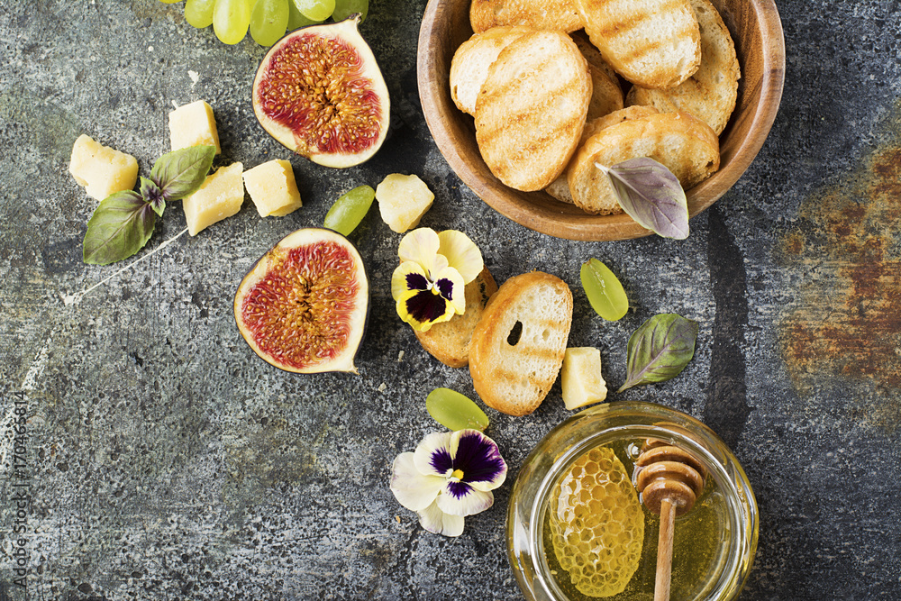 Ingredients for appetizing sandwiches for breakfast or snacks from grilled bread, figs, cheese, grapes, honey and nuts on a gray stone background with edible flowers. Top view.