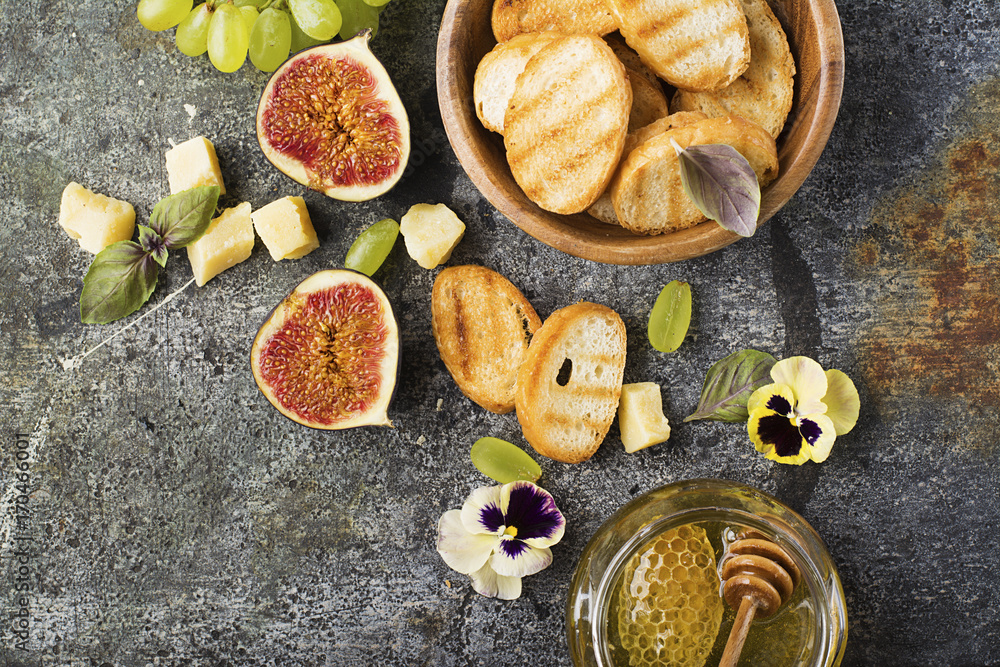 Ingredients for appetizing sandwiches for breakfast or snacks from grilled bread, figs, cheese, grapes, honey and nuts on a gray stone background with edible flowers. Top view. Ingredients for appetizing sandwiches for breakfast or snacks from grilled bread, figs, cheese, grapes, honey and nuts on a gray stone background with edible flowers. Top view.