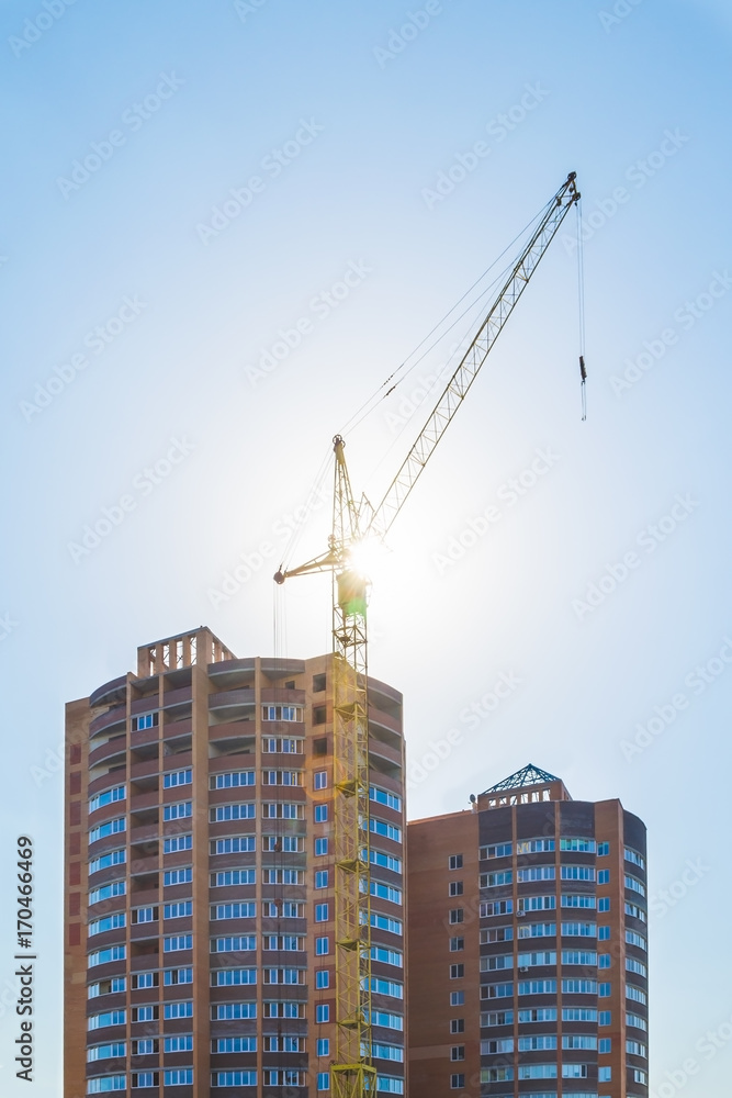 Building crane and building under construction against a blue sky in the sunlight