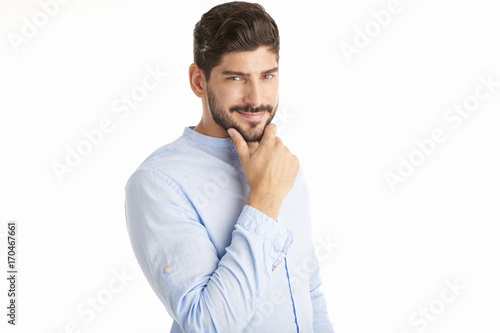 Thinking young man with hand on chin standing against at isolated white background and looking at camera.