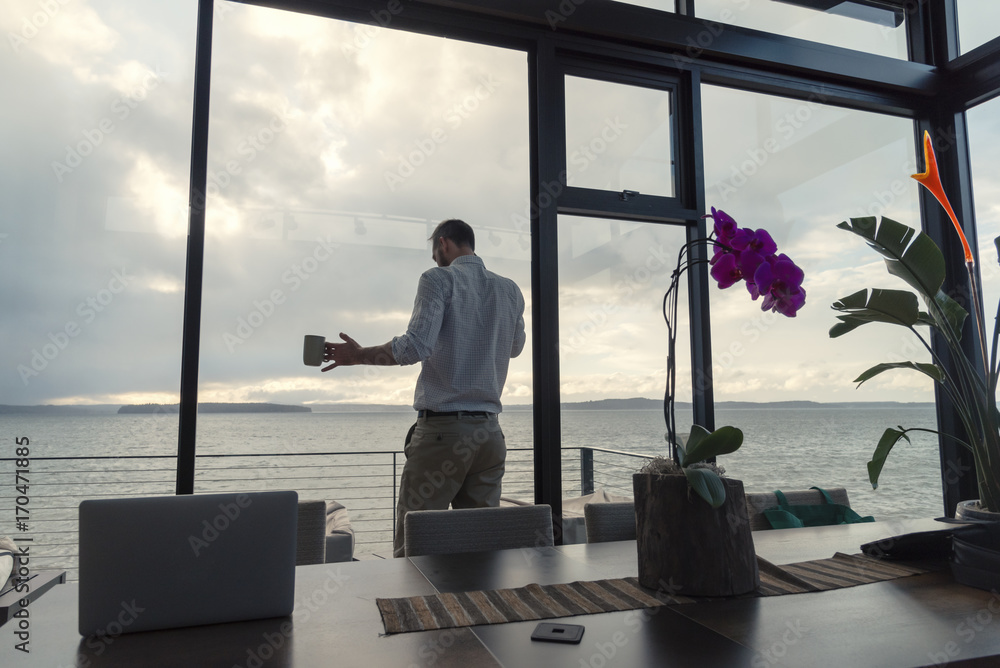 Rear view of man holding coffee mug while talking on the phone in his window view office Rear view of man holding coffee mug while talking on the phone in his window view office
