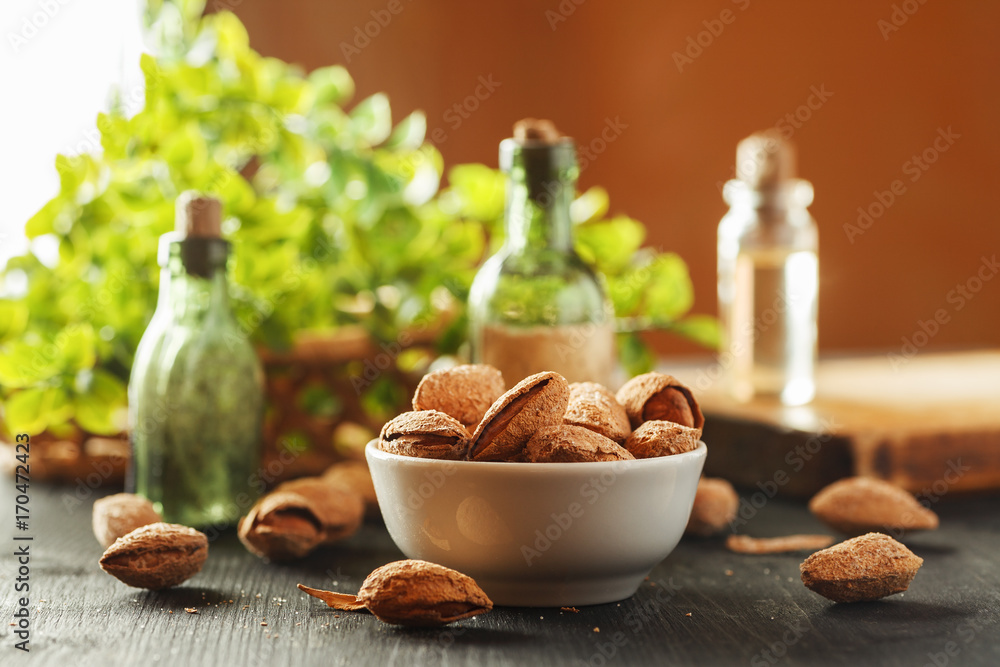 Almond in shell in a white ceramic bowl on a black wooden table with vintage glass bottles and greenery in the background, kitchen composition Almond in shell in a white ceramic bowl on a black wooden table with vintage glass bottles and greenery in the background, kitchen composition