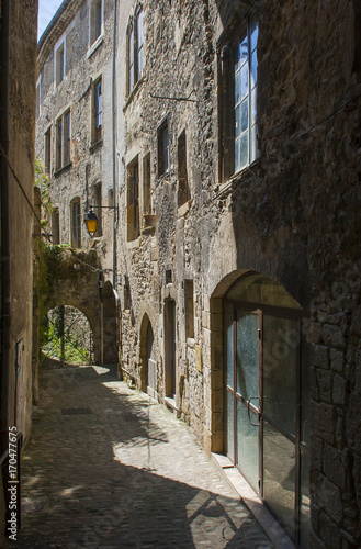 Fototapeta Naklejka Na Ścianę i Meble -  A typical narrow alleyway in the city of Montelimar in France with tall stone buildings and doorways with dark shadows