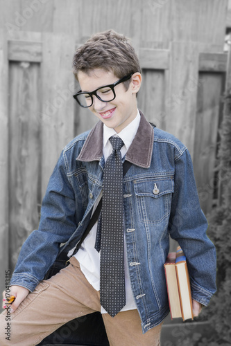 Young preteen boy smiling, holding books, pencils and leather bag outdoors, ready for school